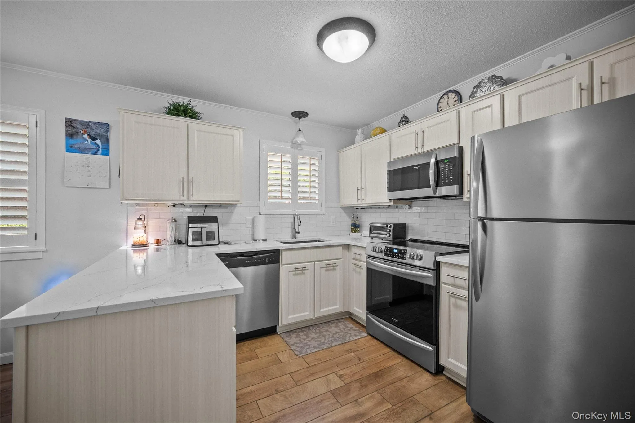 Kitchen featuring white shaker-style cabinetry, stainless steel appliances, ceramic flooring, white subway tile backsplash, and white plantation shutters Kitchen featuring white shaker-style cabinetry, stainless steel appliances, ceramic flooring, white subway tile backsplash, and white plantation shutters