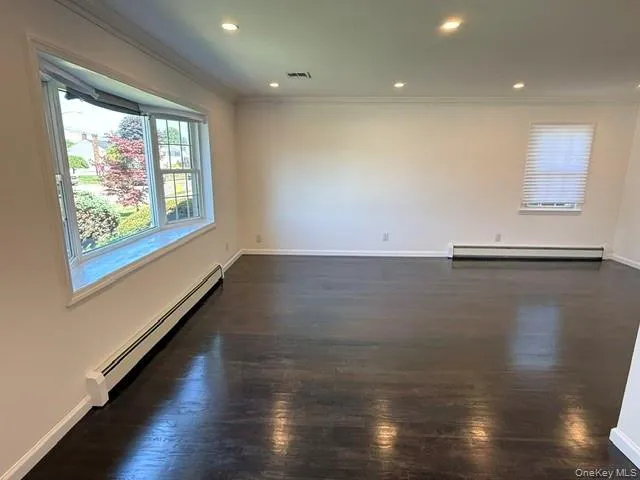 Spacious interior room featuring dark wood-finish flooring, white walls, and a large bay window Spacious interior room featuring dark wood-finish flooring, white walls, and a large bay window