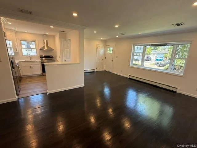 Spacious living area featuring dark wood-finish flooring, recessed lighting, and a large front-facing window Spacious living area featuring dark wood-finish flooring, recessed lighting, and a large front-facing window