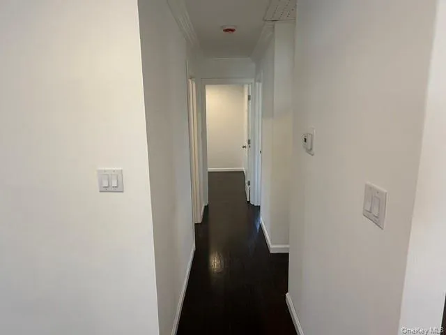 Hallway featuring dark wood-finish flooring, white walls, and white baseboards Hallway featuring dark wood-finish flooring, white walls, and white baseboards
