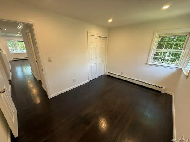 Spacious room featuring dark wood-finish flooring, recessed lighting, and a window with white trim Spacious room featuring dark wood-finish flooring, recessed lighting, and a window with white trim