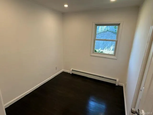 Room featuring wood-finish flooring, white baseboards, and bright recessed lighting Room featuring wood-finish flooring, white baseboards, and bright recessed lighting