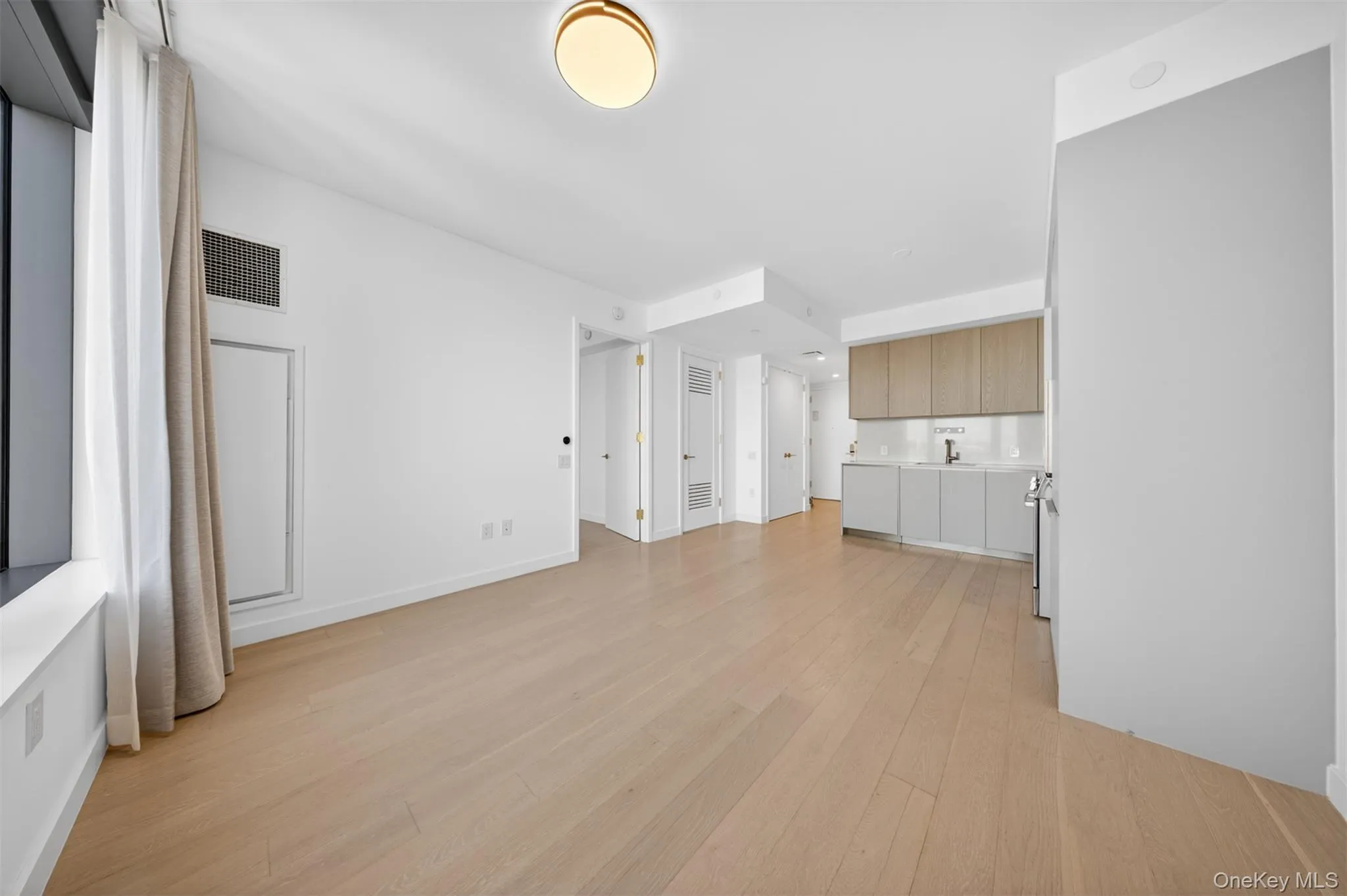 Open-concept living area with light wood-finish flooring, recessed ceiling lighting, and a modern flush-mount light fixture Open-concept living area with light wood-finish flooring, recessed ceiling lighting, and a modern flush-mount light fixture