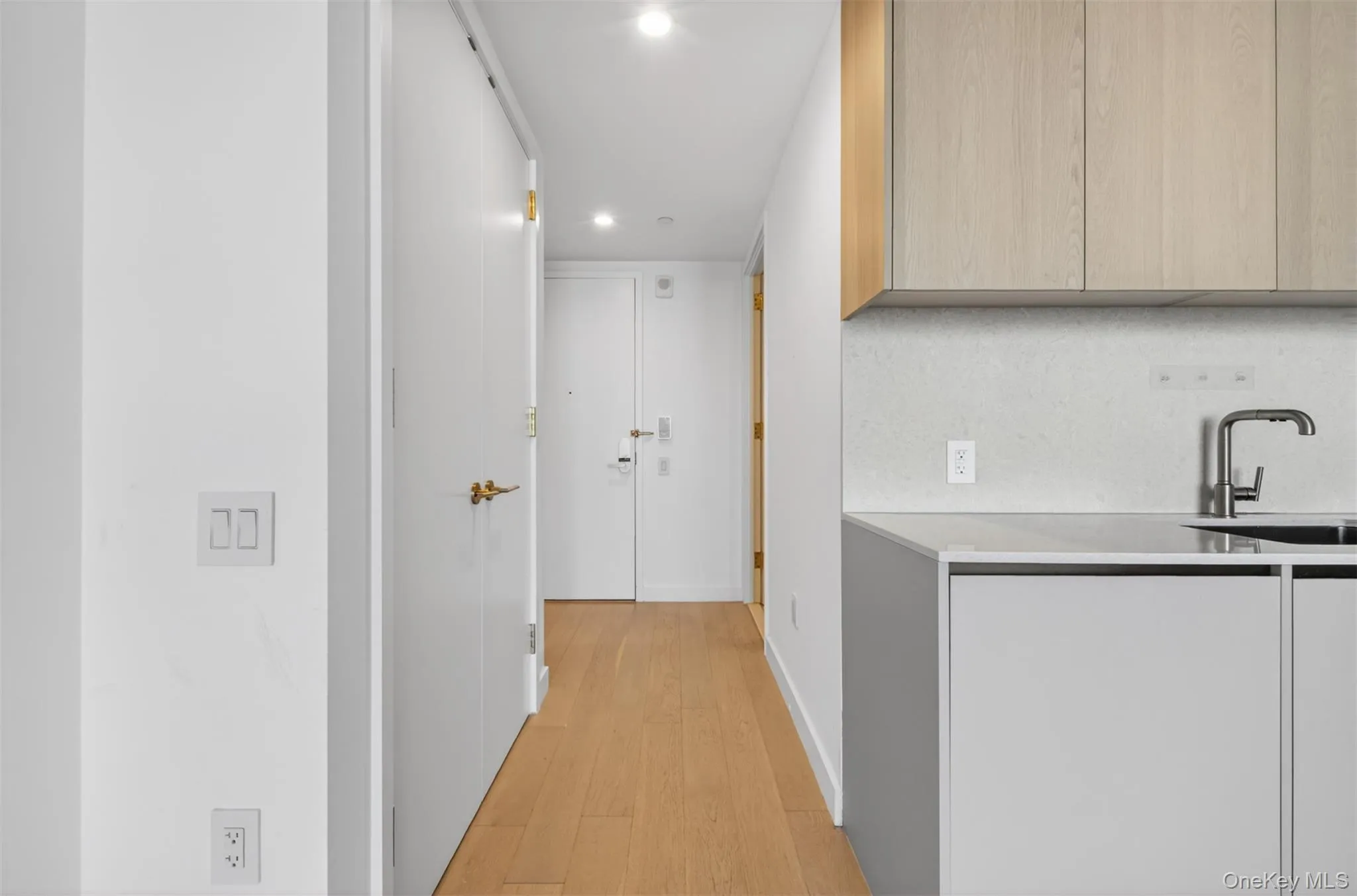 Streamlined kitchen area featuring light wood-finish cabinetry, a solid surface countertop, and a contemporary sink with a gooseneck faucet Streamlined kitchen area featuring light wood-finish cabinetry, a solid surface countertop, and a contemporary sink with a gooseneck faucet