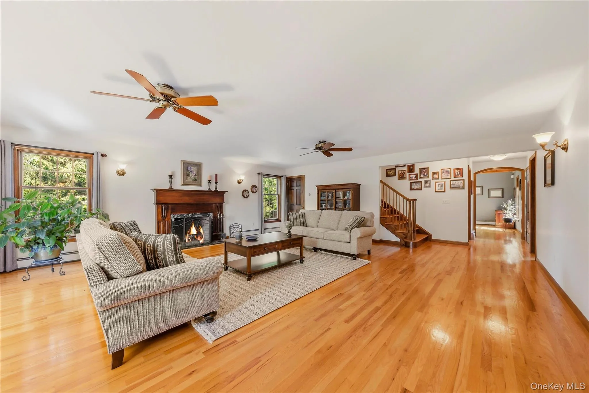 Expansive living area featuring wood-finish flooring, a wood-burning fireplace with an ornate mantel, and multiple ceiling fans Expansive living area featuring wood-finish flooring, a wood-burning fireplace with an ornate mantel, and multiple ceiling fans