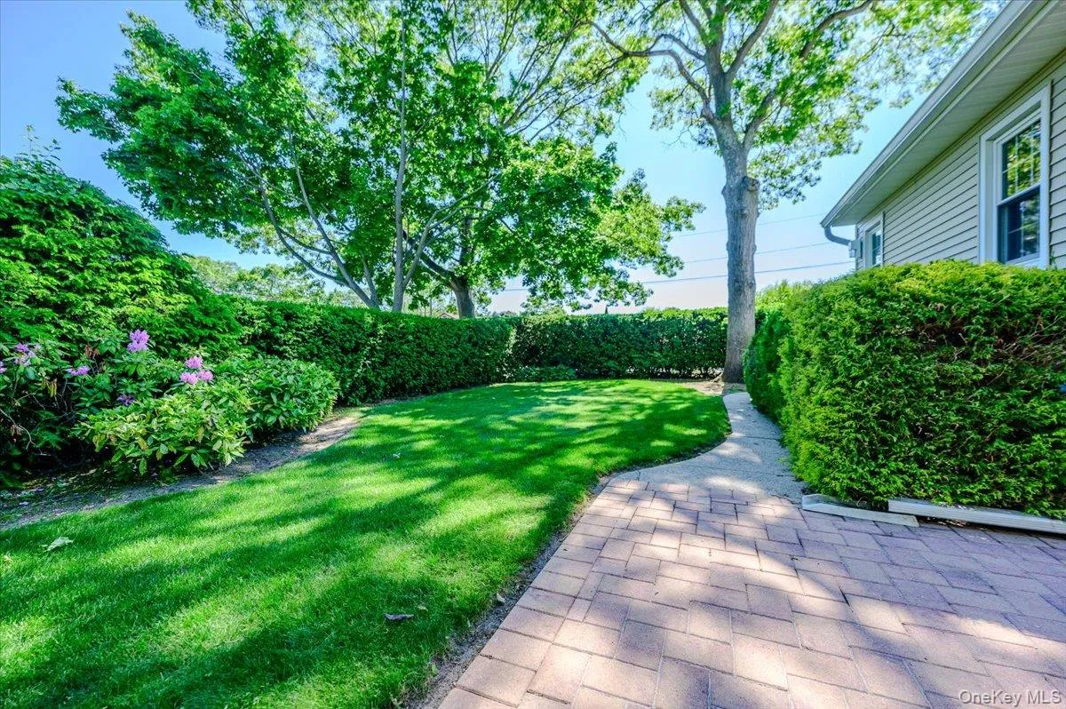 Expansive rear yard featuring a manicured lawn, established privacy hedges, mature trees, and a paver stone pathway Expansive rear yard featuring a manicured lawn, established privacy hedges, mature trees, and a paver stone pathway