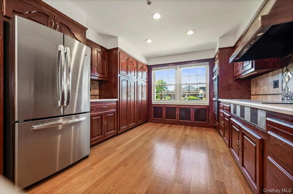 Kitchen featuring rich wood cabinetry, stainless steel refrigerator, light wood-finish flooring, recessed lighting, and a large window. Kitchen featuring rich wood cabinetry, stainless steel refrigerator, light wood-finish flooring, recessed lighting, and a large window.
