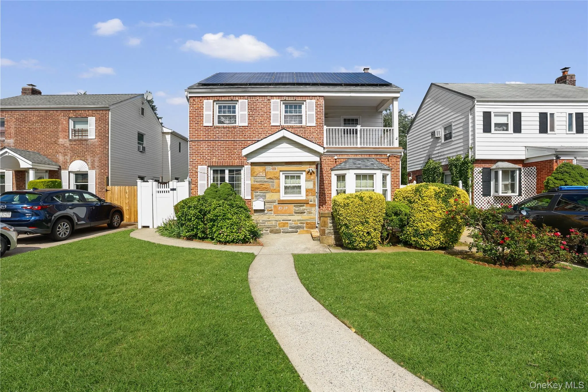 Brick and stone facade residence featuring solar panels, an upper-level balcony with white railing, and a bay window Brick and stone facade residence featuring solar panels, an upper-level balcony with white railing, and a bay window