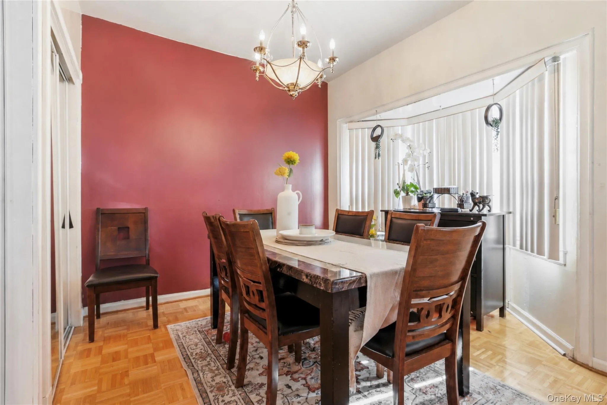 Dining area featuring a prominent red accent wall, parquet wood-finish flooring, and an elegant chandelier Dining area featuring a prominent red accent wall, parquet wood-finish flooring, and an elegant chandelier