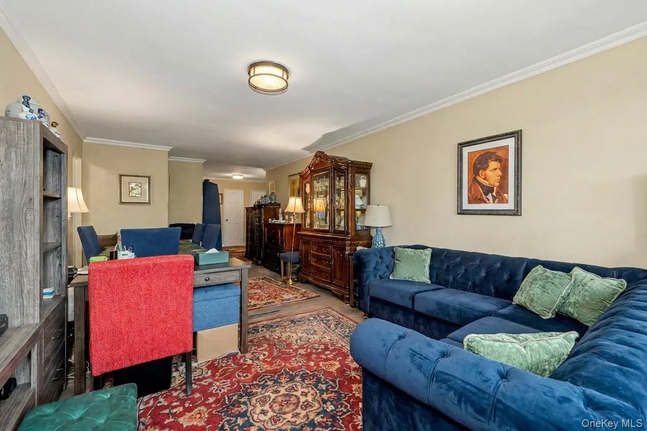 Open concept living space featuring a deep blue upholstered sectional, crown molding, and wood-finish flooring, Virtually Enhanced. Open concept living space featuring a deep blue upholstered sectional, crown molding, and wood-finish flooring, Virtually Enhanced.