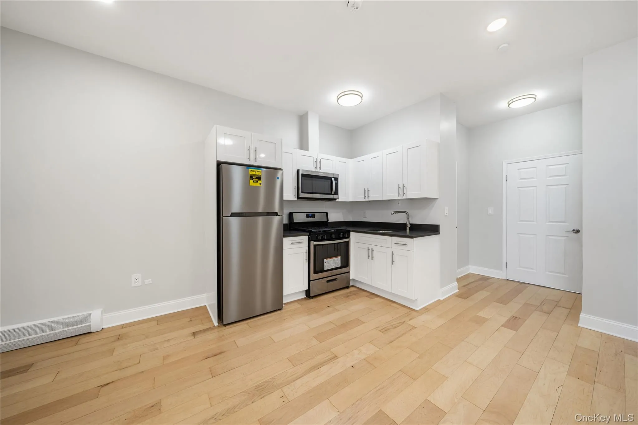 Open-concept living space featuring wood-finish flooring, white cabinetry, stainless steel appliances, and dark countertops Open-concept living space featuring wood-finish flooring, white cabinetry, stainless steel appliances, and dark countertops