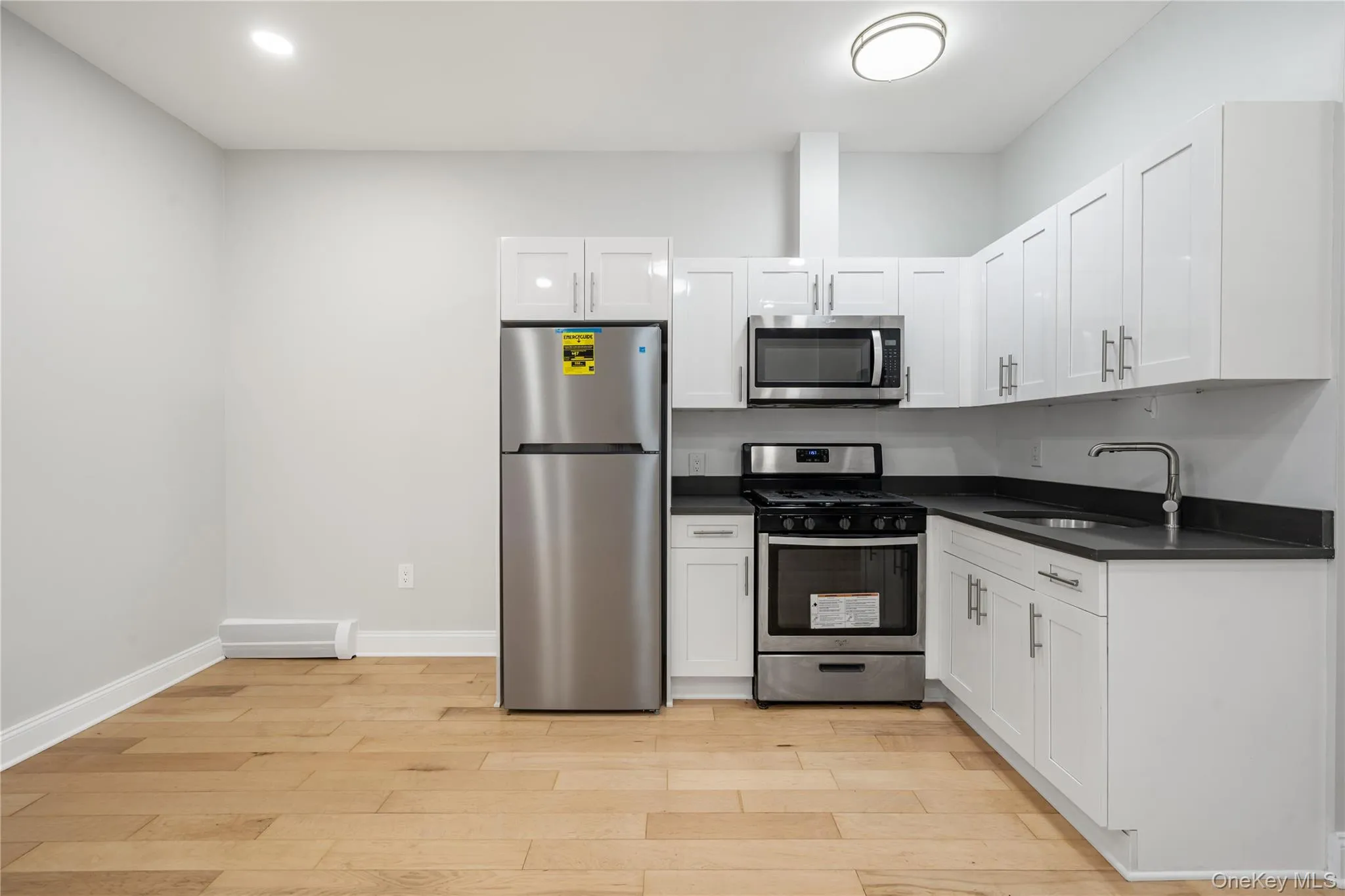 Modern kitchen featuring white cabinetry, dark countertops, and stainless steel appliances including a refrigerator, range, and microwave Modern kitchen featuring white cabinetry, dark countertops, and stainless steel appliances including a refrigerator, range, and microwave