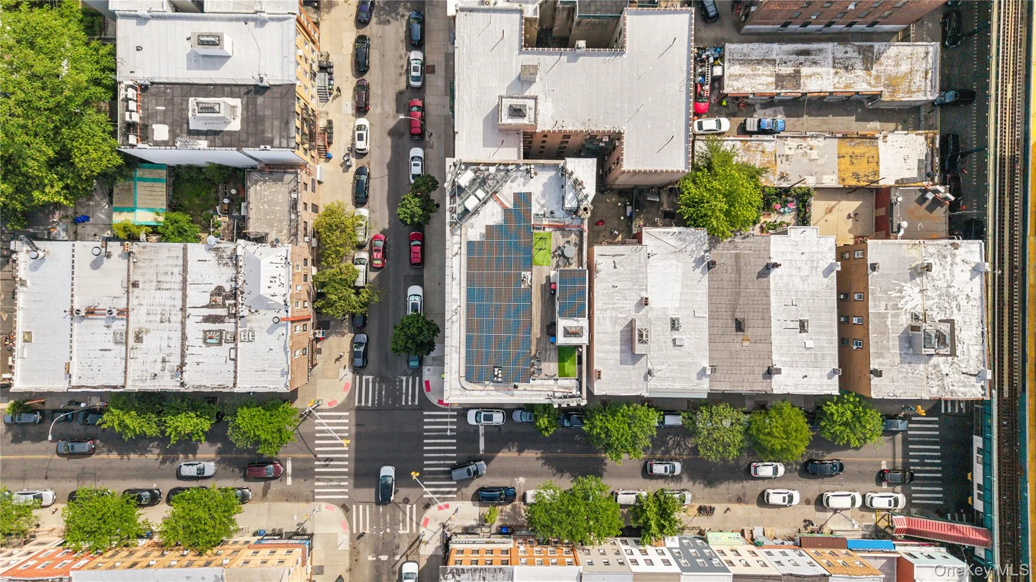 Aerial perspective of an urban neighborhood featuring street-level parking, established street trees, and a building with rooftop solar panels Aerial perspective of an urban neighborhood featuring street-level parking, established street trees, and a building with rooftop solar panels