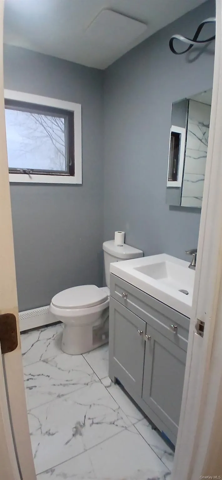 Half bath with vanity, light marble finish flooring, and baseboard heating Half bath with vanity, light marble finish flooring, and baseboard heating