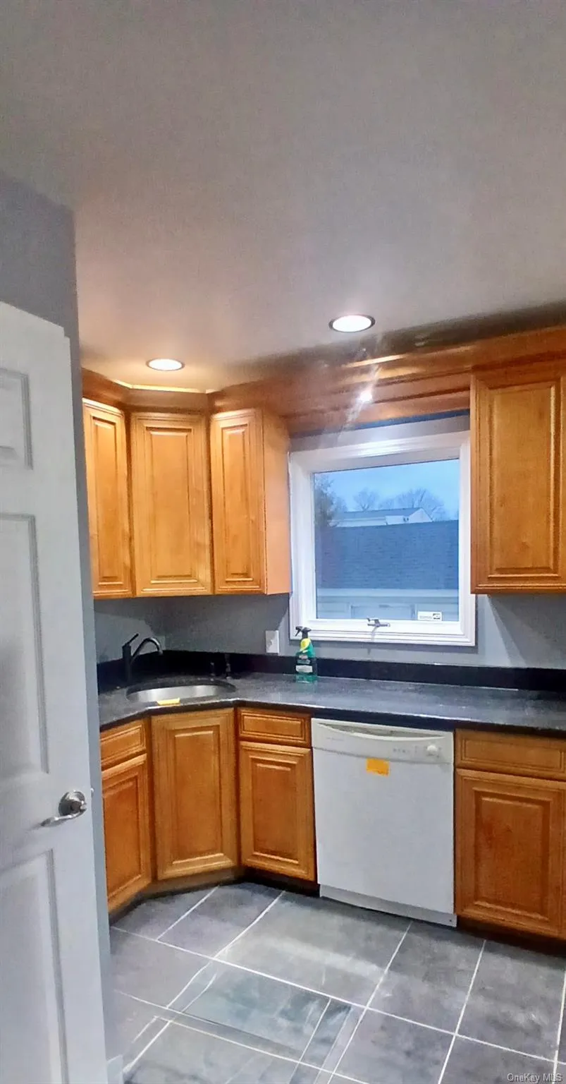Kitchen featuring dishwasher, dark tile patterned floors, brown cabinetry, and recessed lighting Kitchen featuring dishwasher, dark tile patterned floors, brown cabinetry, and recessed lighting