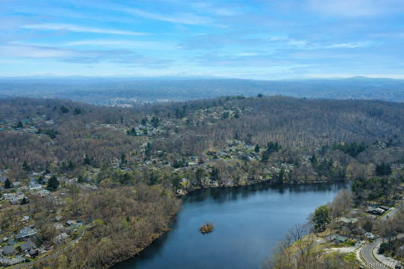 Aerial view of the surrounding area featuring a body of water, extensive tree coverage, and distant hills under a clear sky Aerial view of the surrounding area featuring a body of water, extensive tree coverage, and distant hills under a clear sky