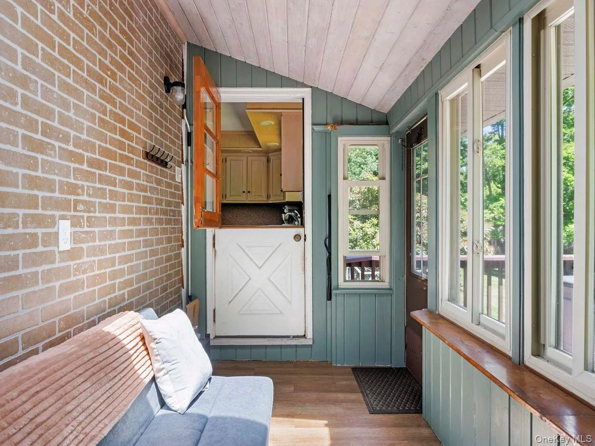 Enclosed porch featuring a light brick wall, wood-finish flooring, and a whitewashed wood-paneled ceiling Enclosed porch featuring a light brick wall, wood-finish flooring, and a whitewashed wood-paneled ceiling