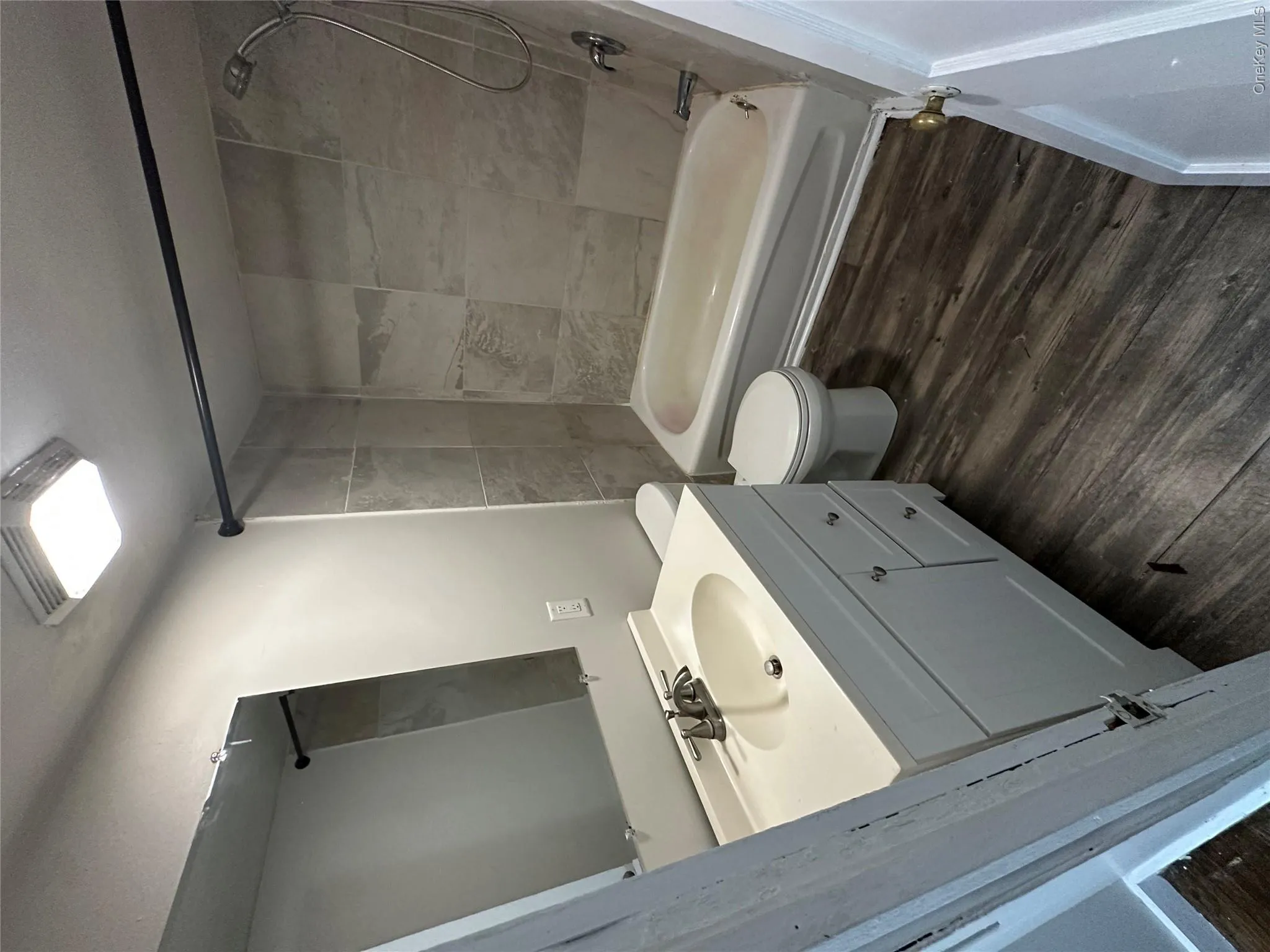 Bathroom featuring wood-finish flooring, a white vanity with a single basin sink, a wall-mounted mirror, and a bathtub with light-colored tile surround Bathroom featuring wood-finish flooring, a white vanity with a single basin sink, a wall-mounted mirror, and a bathtub with light-colored tile surround