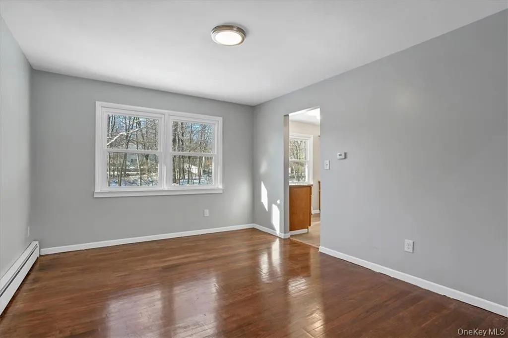 Unfurnished room featuring baseboard heating and dark wood finished floors Unfurnished room featuring baseboard heating and dark wood finished floors