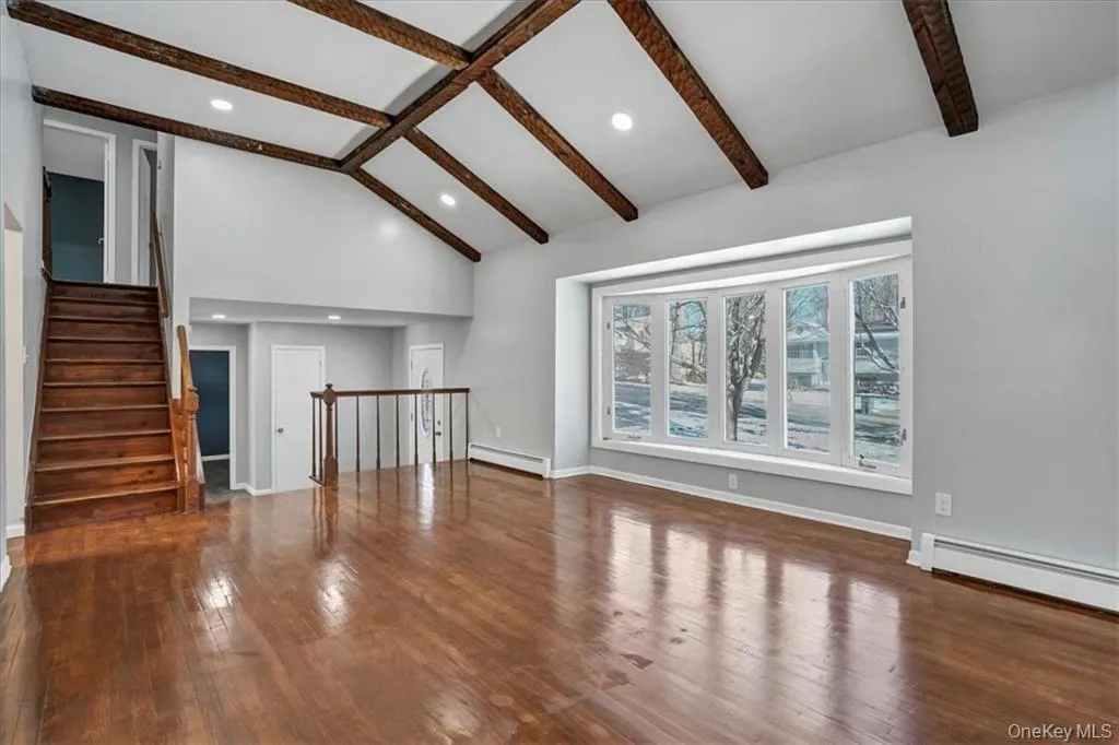 Unfurnished living room with beamed ceiling, dark wood finished floors, stairway, recessed lighting, and baseboard heating Unfurnished living room with beamed ceiling, dark wood finished floors, stairway, recessed lighting, and baseboard heating