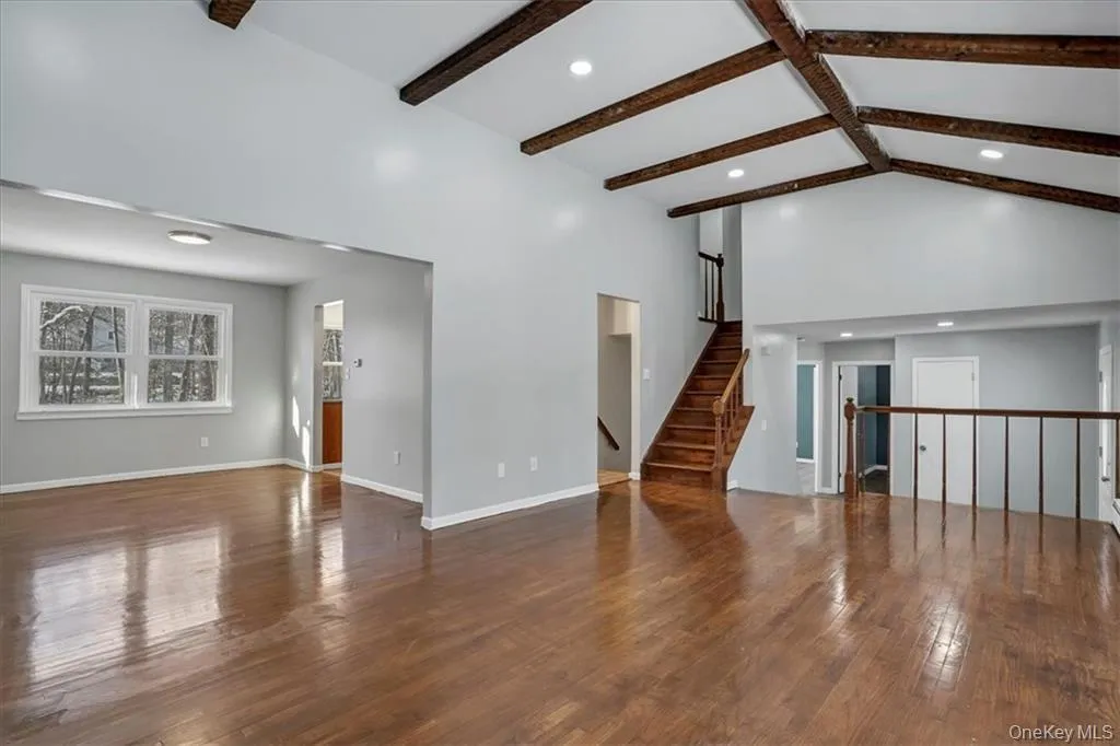 Unfurnished living room featuring dark wood-style floors, beamed ceiling, high vaulted ceiling, recessed lighting, and stairs Unfurnished living room featuring dark wood-style floors, beamed ceiling, high vaulted ceiling, recessed lighting, and stairs