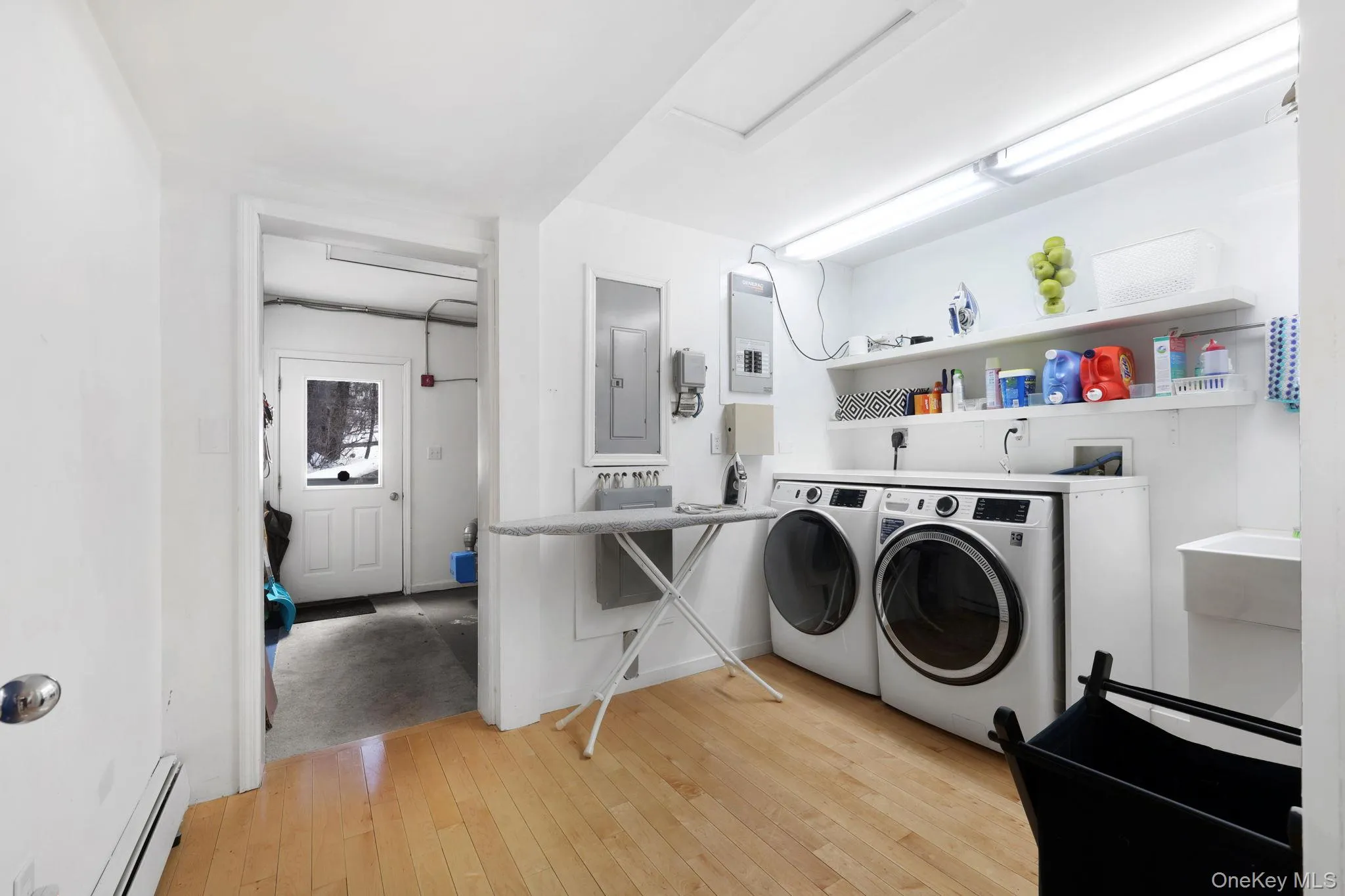 Laundry area featuring a baseboard radiator, electric panel, light wood-style flooring, and washing machine and dryer Laundry area featuring a baseboard radiator, electric panel, light wood-style flooring, and washing machine and dryer