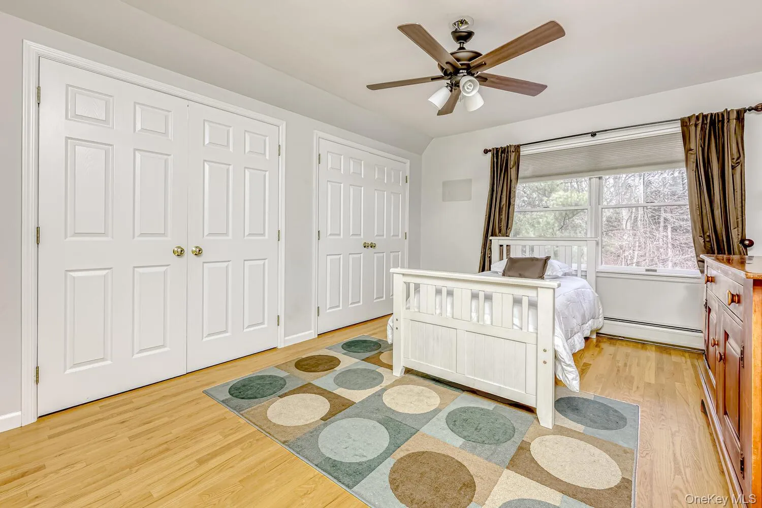 Bedroom with light wood finished floors, two closets, baseboard heating, and ceiling fan Bedroom with light wood finished floors, two closets, baseboard heating, and ceiling fan