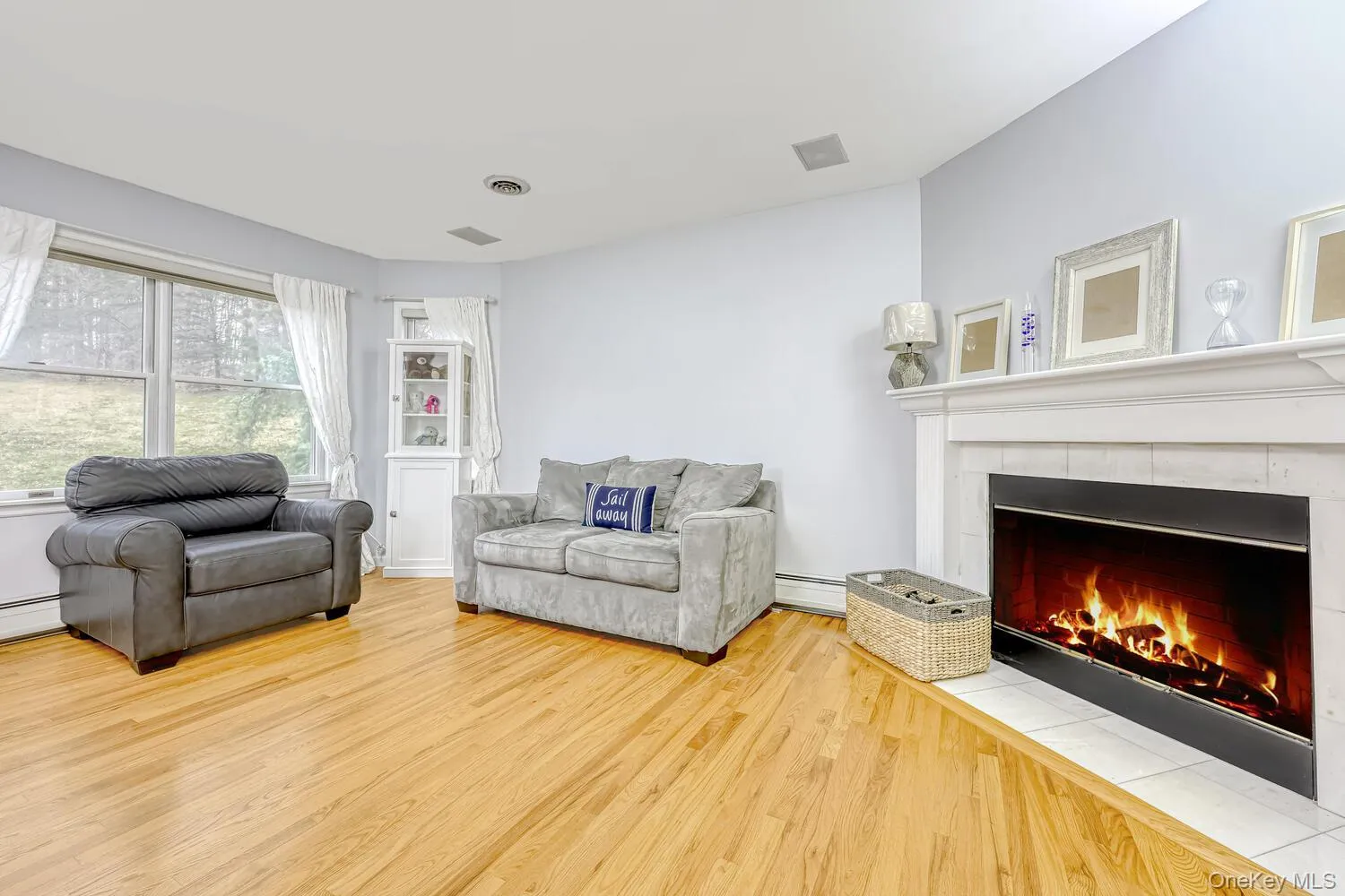 Living area with a tiled fireplace, light wood-style flooring, and a baseboard radiator Living area with a tiled fireplace, light wood-style flooring, and a baseboard radiator