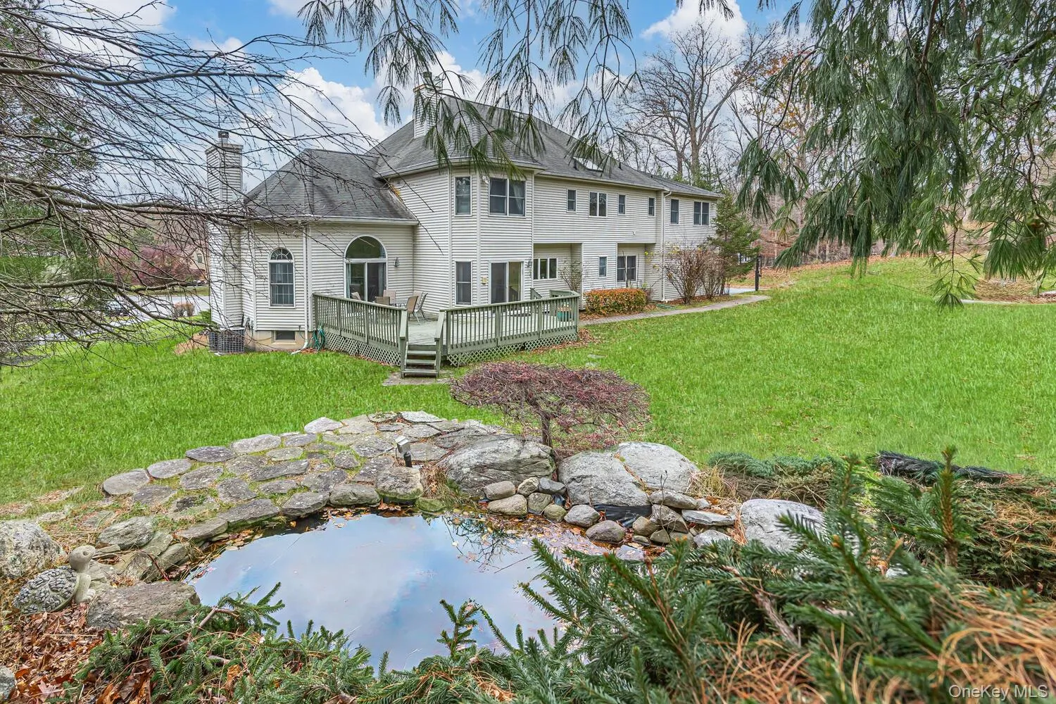 Rear view of property with a lawn, a chimney, a wooden deck, and a small pond Rear view of property with a lawn, a chimney, a wooden deck, and a small pond