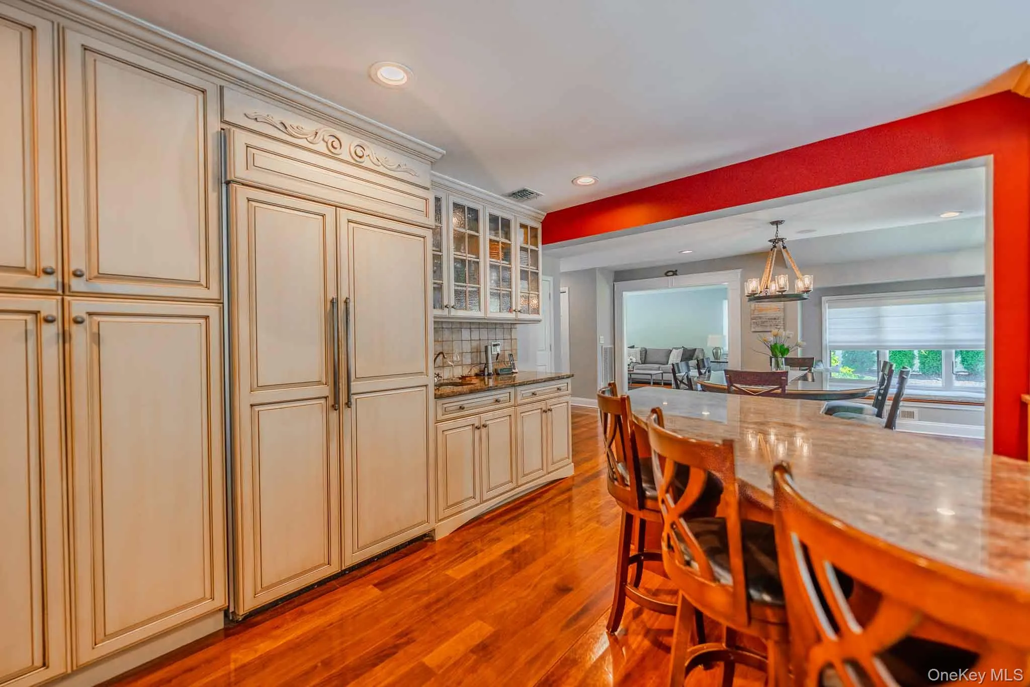 Kitchen featuring integrated paneled refrigerator, built-in cabinetry with glass-front uppers, polished wood-finish flooring, and a curved island with a granite countertop Kitchen featuring integrated paneled refrigerator, built-in cabinetry with glass-front uppers, polished wood-finish flooring, and a curved island with a granite countertop