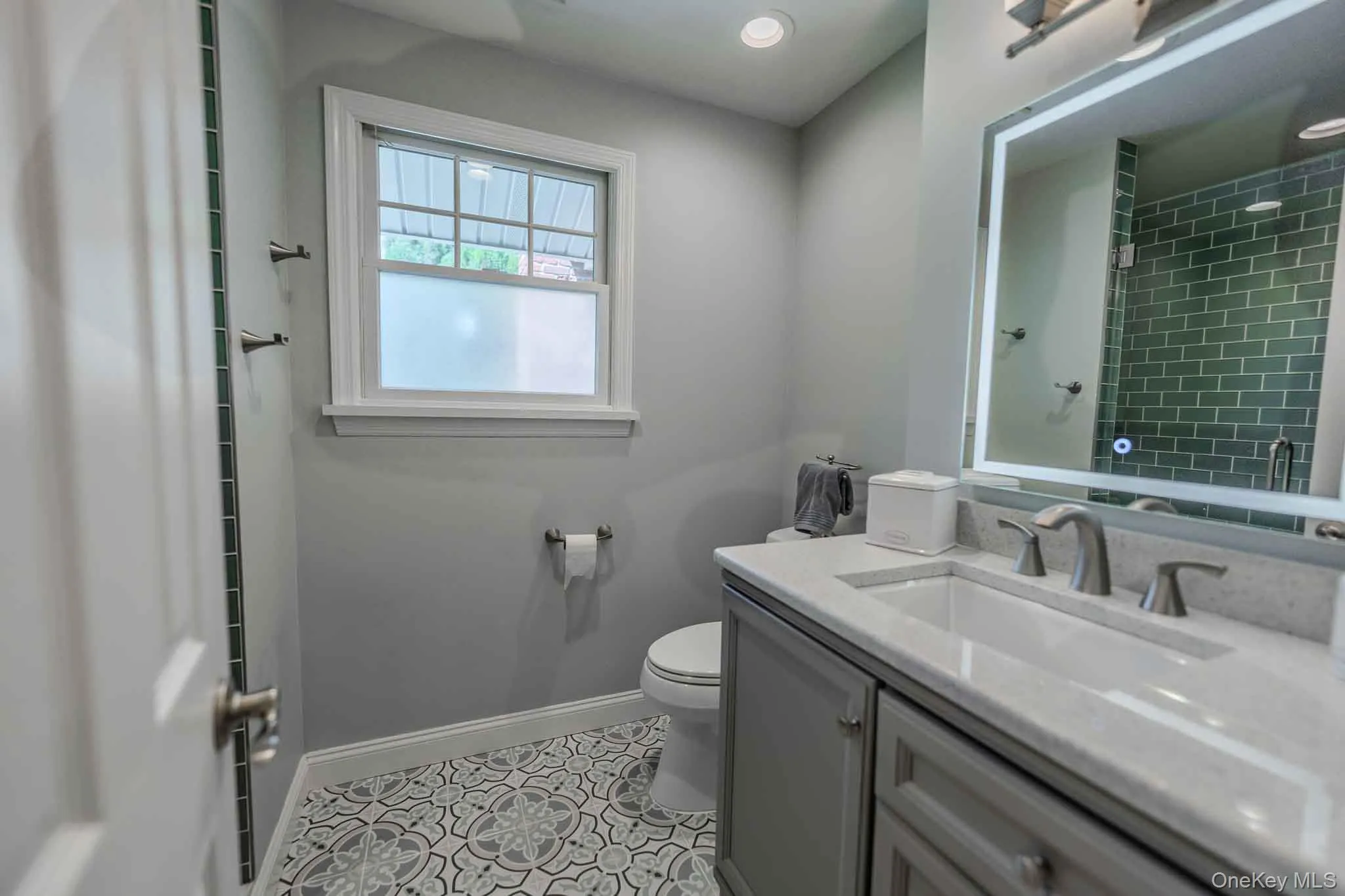 Stylishly renovated bathroom featuring a contemporary vanity, an illuminated LED mirror, beautiful teal accent tiling, and eye-catching patterned tile flooring. Stylishly renovated bathroom featuring a contemporary vanity, an illuminated LED mirror, beautiful teal accent tiling, and eye-catching patterned tile flooring.