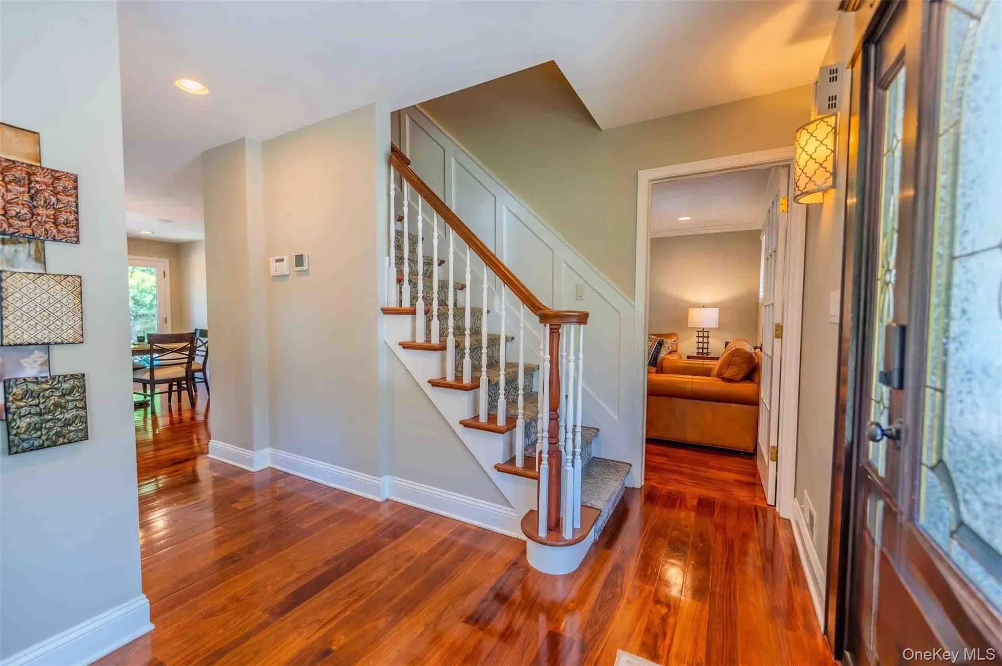 Warm and inviting entry foyer showcasing stunning gleaming hardwood floors, a beautiful wood-rail staircase, and an open layout that leads seamlessly into the main living spaces. Warm and inviting entry foyer showcasing stunning gleaming hardwood floors, a beautiful wood-rail staircase, and an open layout that leads seamlessly into the main living spaces.