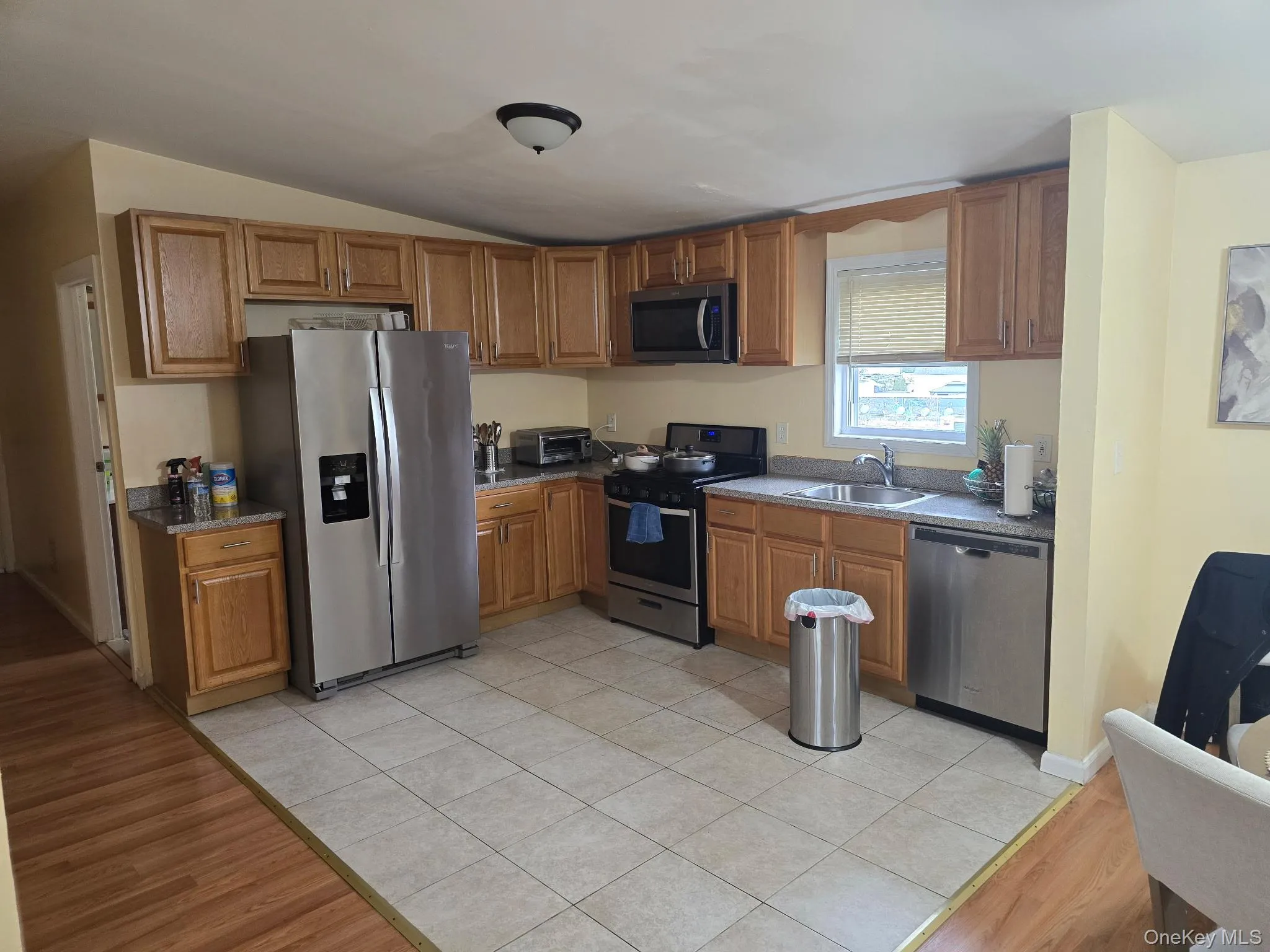 Kitchen featuring light wood-type flooring, stainless steel appliances, brown cabinetry, and vaulted ceiling Kitchen featuring light wood-type flooring, stainless steel appliances, brown cabinetry, and vaulted ceiling