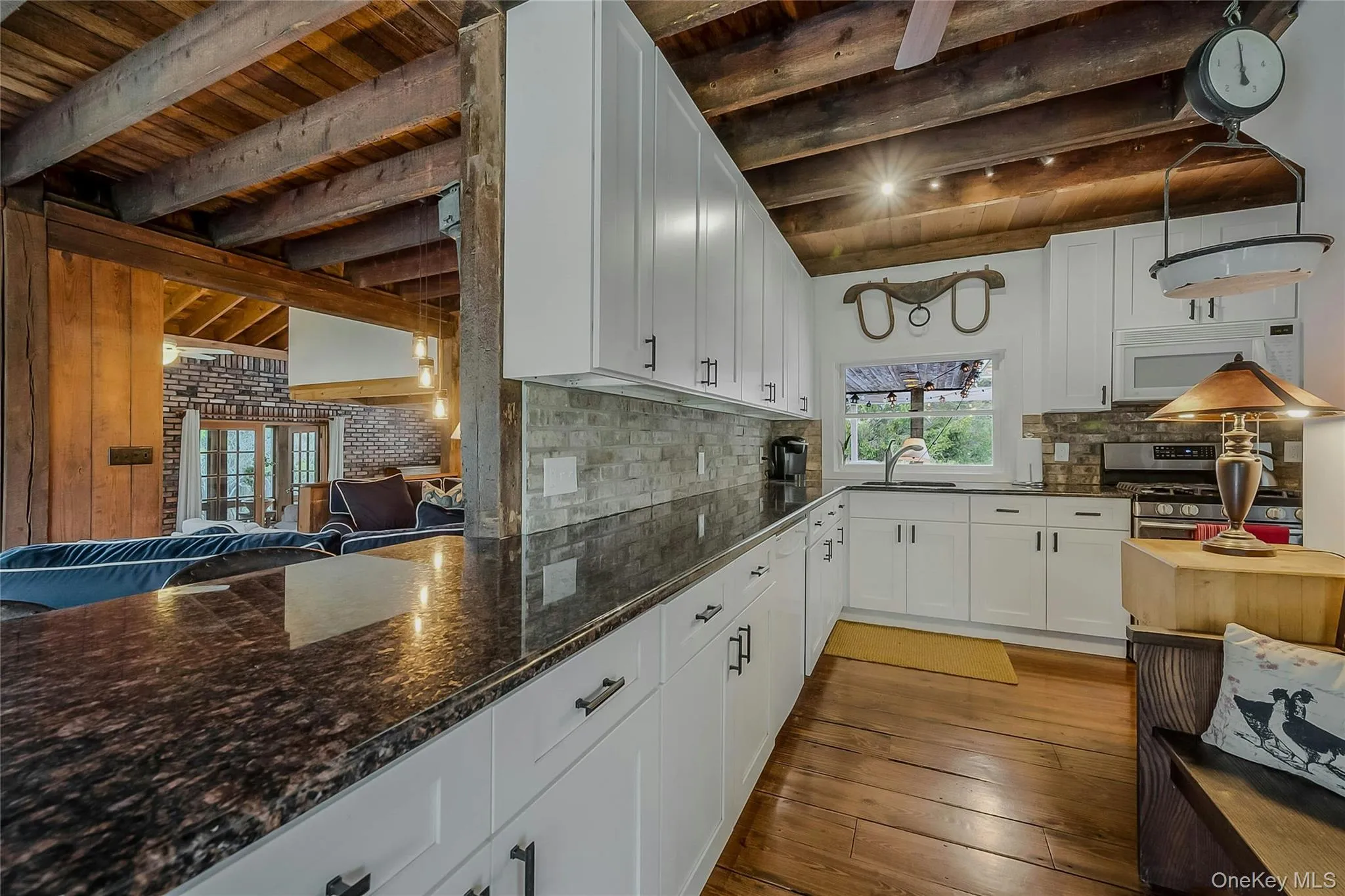 Kitchen featuring white microwave, wood ceiling with exposed beams, stainless steel range with gas cooktop, a sink, and light wood finished floors Kitchen featuring white microwave, wood ceiling with exposed beams, stainless steel range with gas cooktop, a sink, and light wood finished floors
