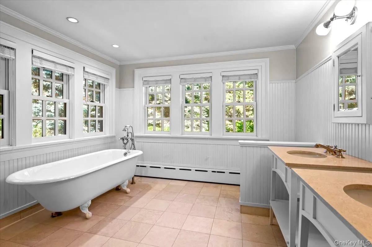 Bathroom featuring a wainscoted wall, a freestanding tub, baseboard heating, crown molding, and plenty of natural light Bathroom featuring a wainscoted wall, a freestanding tub, baseboard heating, crown molding, and plenty of natural light