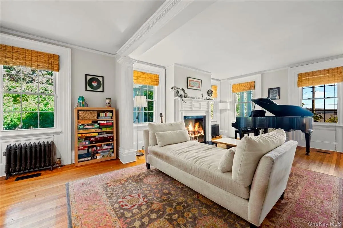 Living room featuring radiator heating unit, healthy amount of natural light, light wood-type flooring, fireplace, and ornamental molding Living room featuring radiator heating unit, healthy amount of natural light, light wood-type flooring, fireplace, and ornamental molding