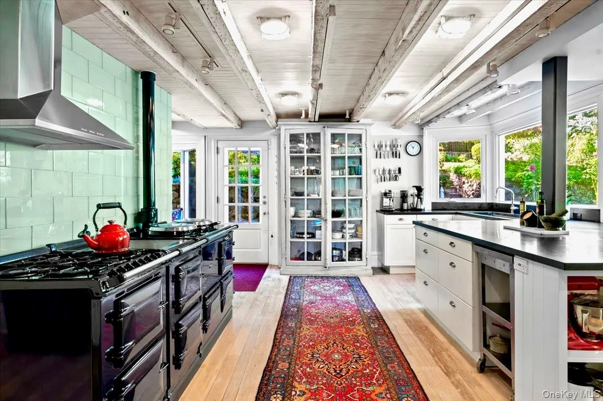 Kitchen featuring wall chimney range hood, beamed ceiling, white cabinetry, light wood-type flooring, and Aga range with two ovens Kitchen featuring wall chimney range hood, beamed ceiling, white cabinetry, light wood-type flooring, and Aga range with two ovens