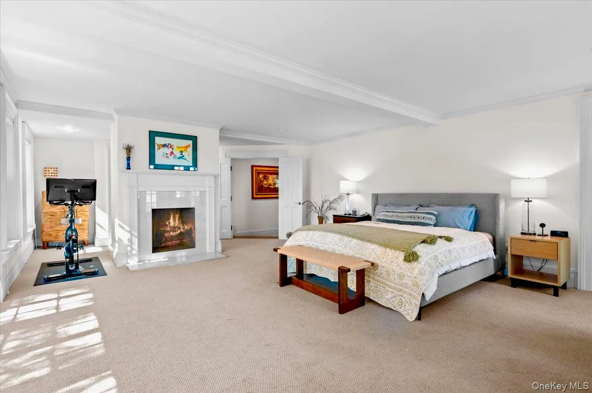Bedroom with carpet, beam ceiling, a warm lit fireplace, and crown molding Bedroom with carpet, beam ceiling, a warm lit fireplace, and crown molding