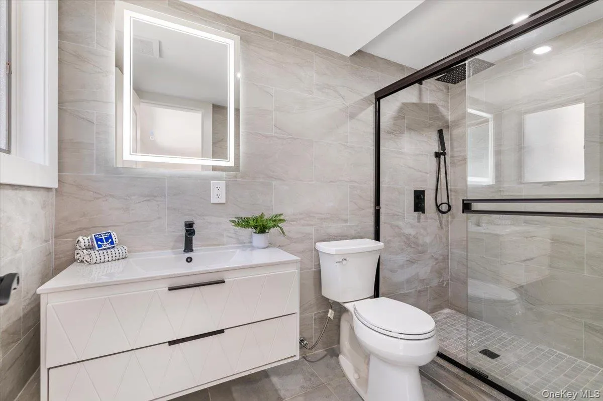Bathroom with tile walls, vanity, a stall shower, and tile patterned flooring Bathroom with tile walls, vanity, a stall shower, and tile patterned flooring