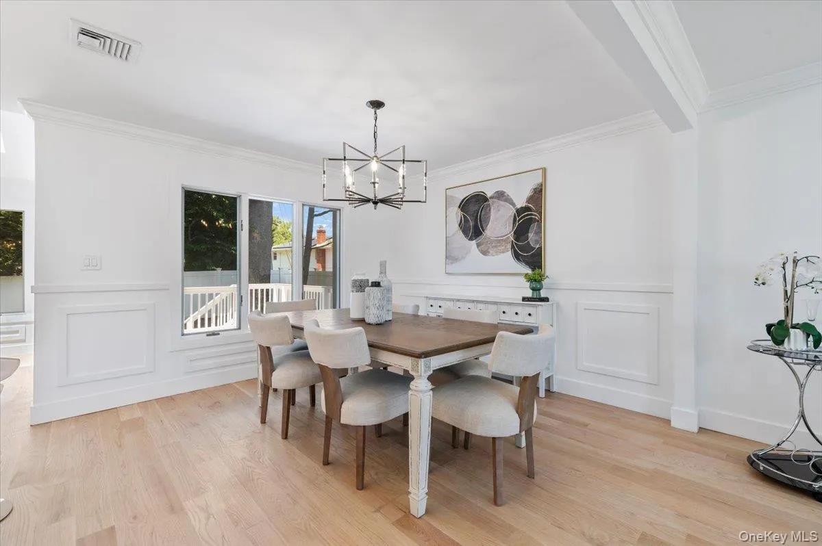 Dining room featuring a chandelier, a decorative wall, ornamental molding, light wood-style flooring, and wainscoting Dining room featuring a chandelier, a decorative wall, ornamental molding, light wood-style flooring, and wainscoting