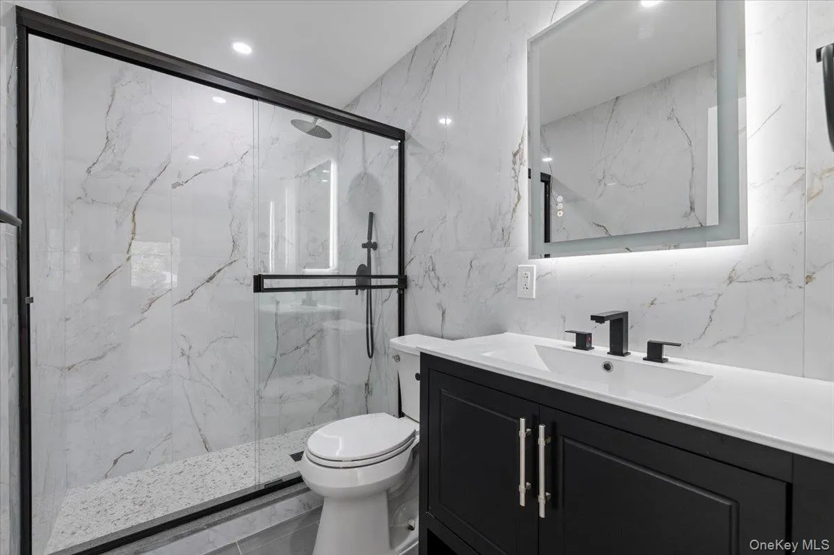 Bathroom featuring vanity, a marble finish shower, tile walls, and recessed lighting Bathroom featuring vanity, a marble finish shower, tile walls, and recessed lighting
