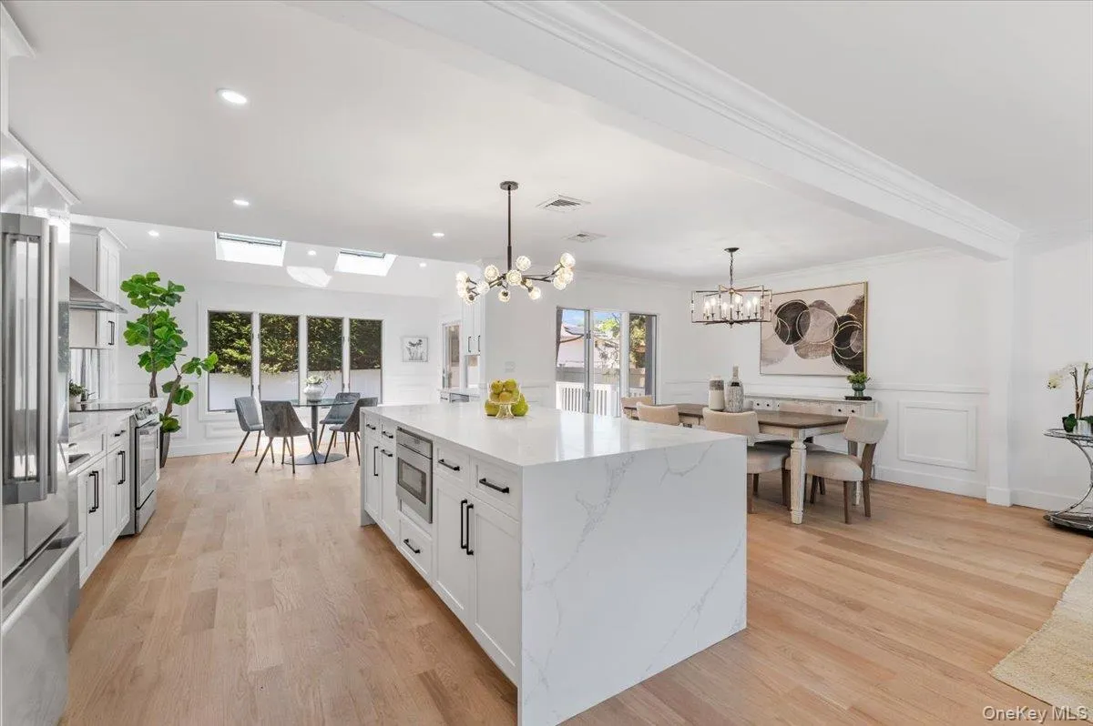 Kitchen featuring a chandelier, stainless steel appliances, white cabinetry, pendant lighting, and light wood finished floors Kitchen featuring a chandelier, stainless steel appliances, white cabinetry, pendant lighting, and light wood finished floors