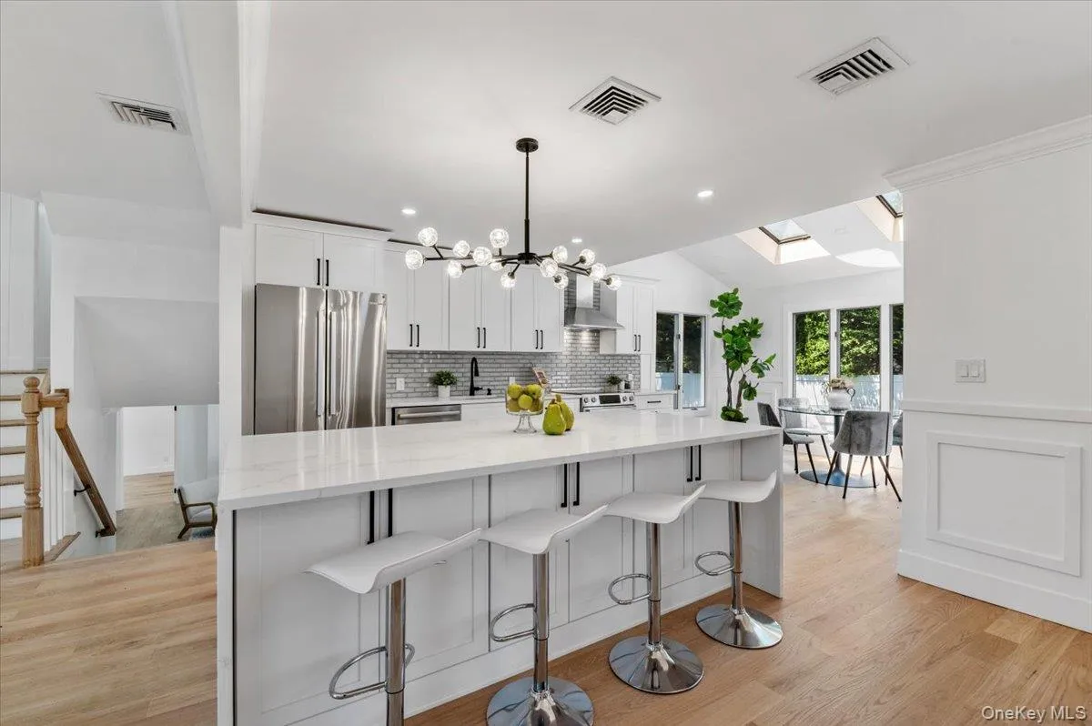 Kitchen featuring freestanding refrigerator, wall chimney range hood, decorative backsplash, white cabinetry, and a skylight Kitchen featuring freestanding refrigerator, wall chimney range hood, decorative backsplash, white cabinetry, and a skylight