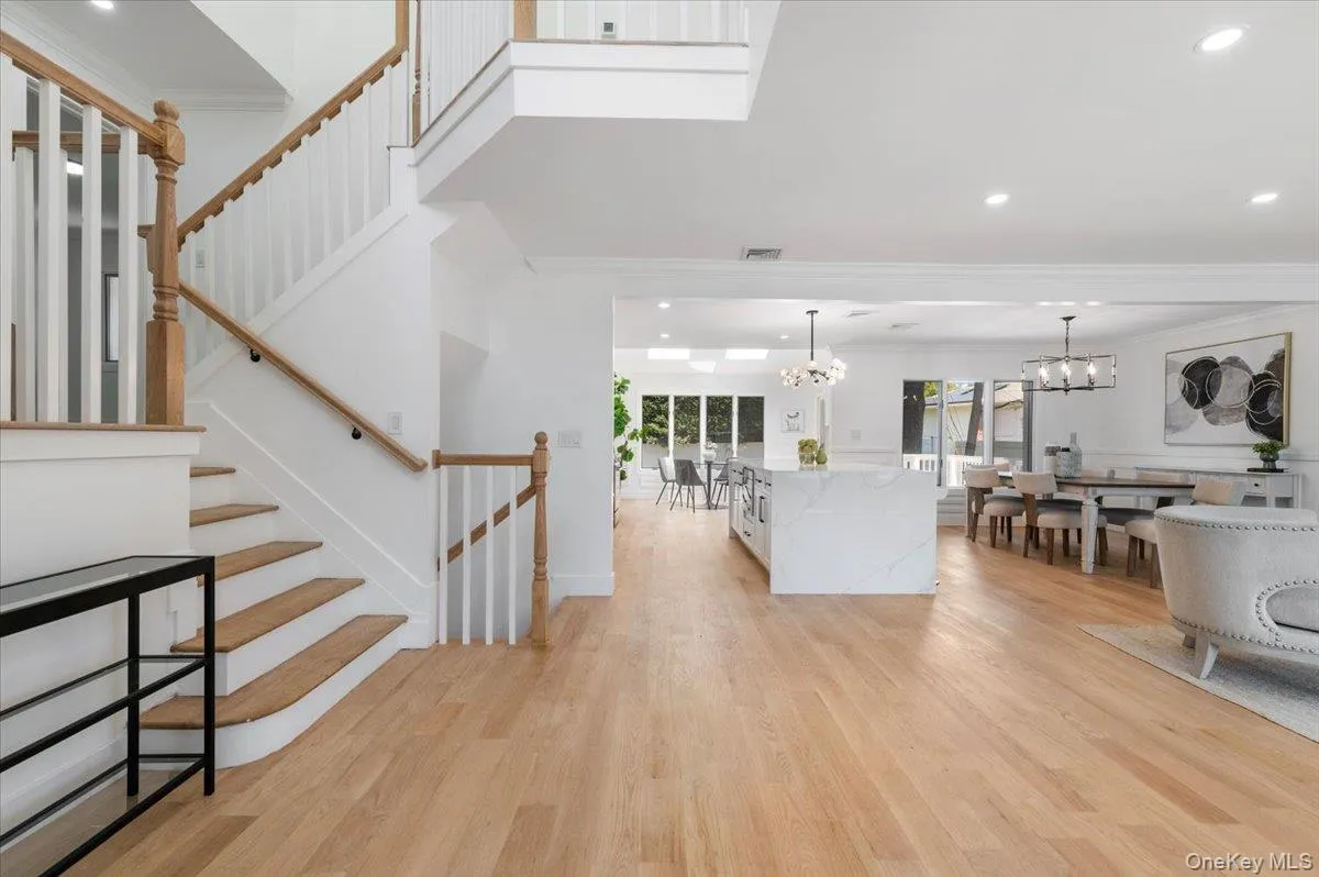Living room with a chandelier, ornamental molding, light wood-type flooring, recessed lighting, and stairs Living room with a chandelier, ornamental molding, light wood-type flooring, recessed lighting, and stairs