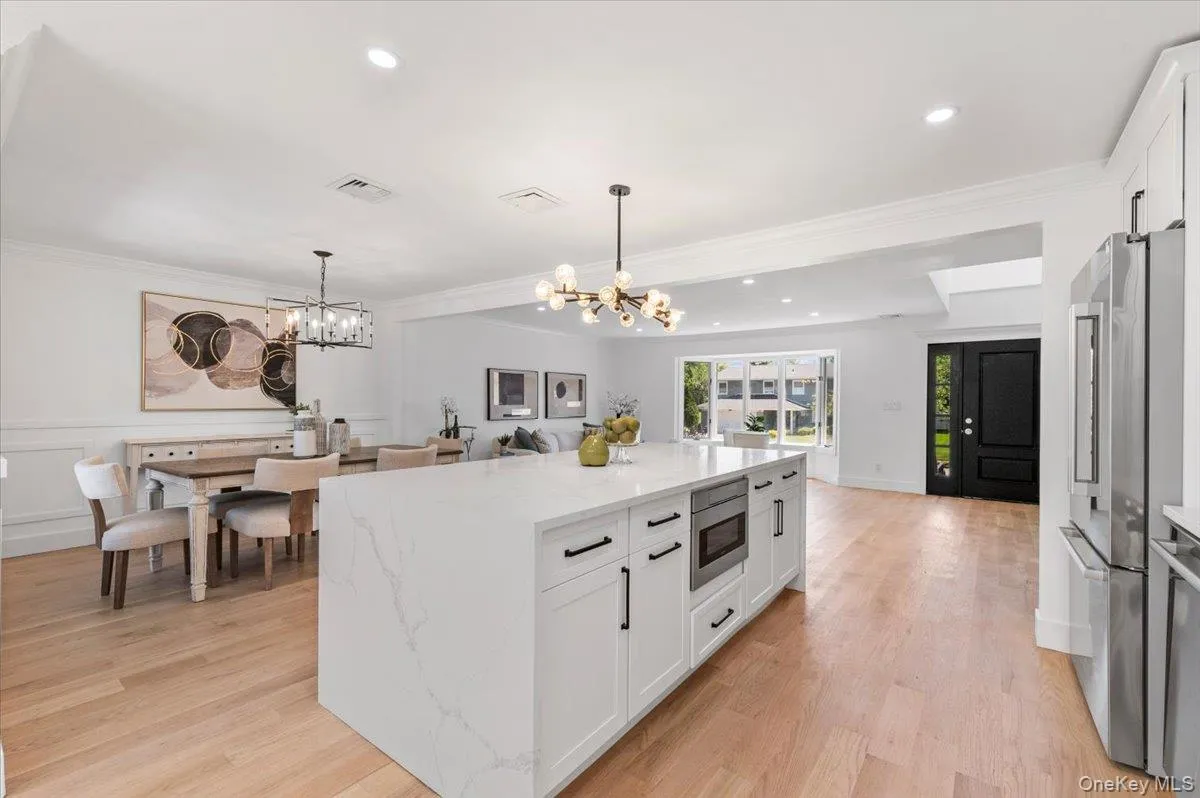 Kitchen featuring a chandelier, appliances with stainless steel finishes, white cabinetry, light stone countertops, and hanging light fixtures Kitchen featuring a chandelier, appliances with stainless steel finishes, white cabinetry, light stone countertops, and hanging light fixtures