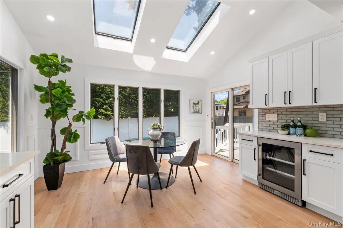 Dining space featuring wine cooler, a decorative wall, a skylight, light wood-style flooring, and a wainscoted wall Dining space featuring wine cooler, a decorative wall, a skylight, light wood-style flooring, and a wainscoted wall