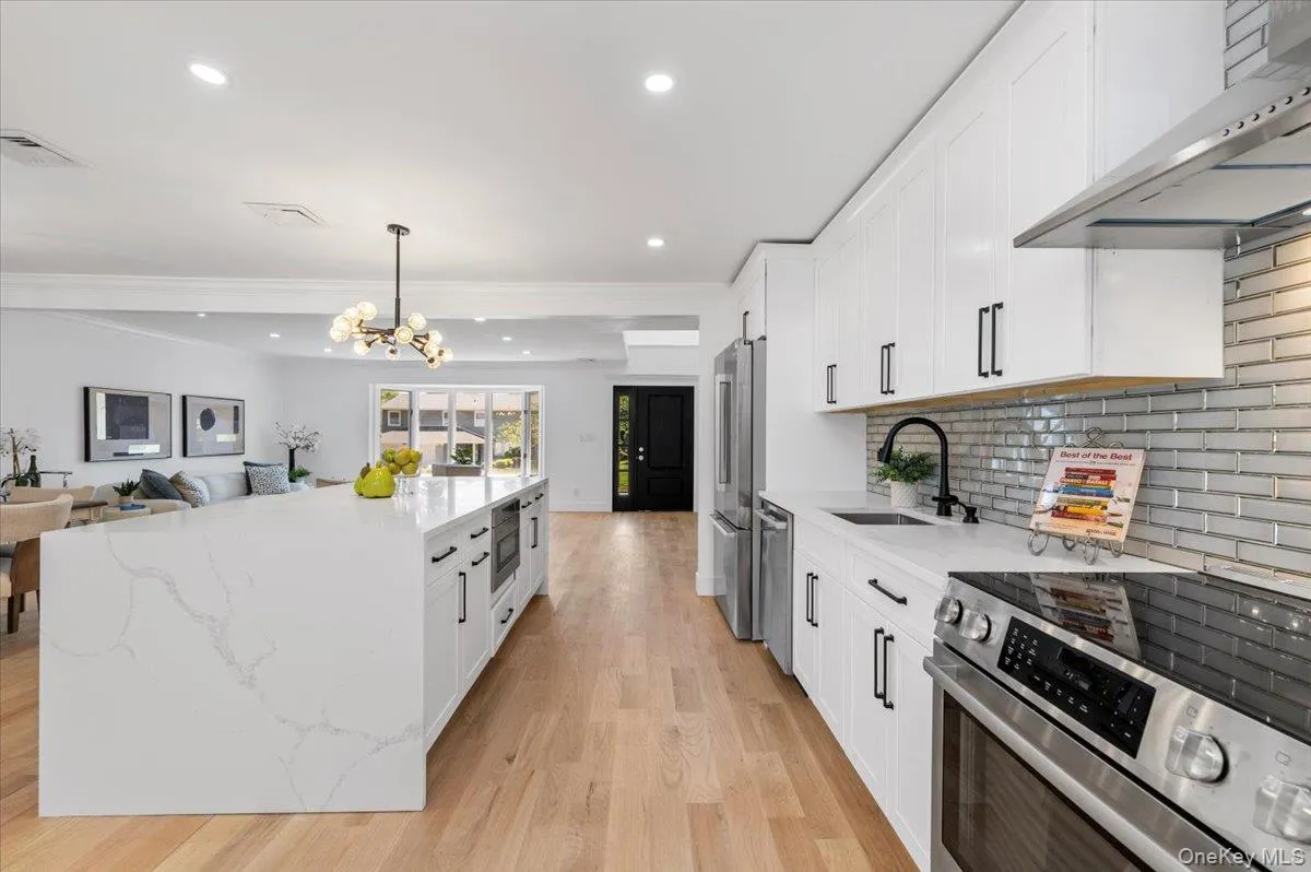 Kitchen featuring appliances with stainless steel finishes, wall chimney exhaust hood, light wood-type flooring, white cabinetry, and crown molding Kitchen featuring appliances with stainless steel finishes, wall chimney exhaust hood, light wood-type flooring, white cabinetry, and crown molding