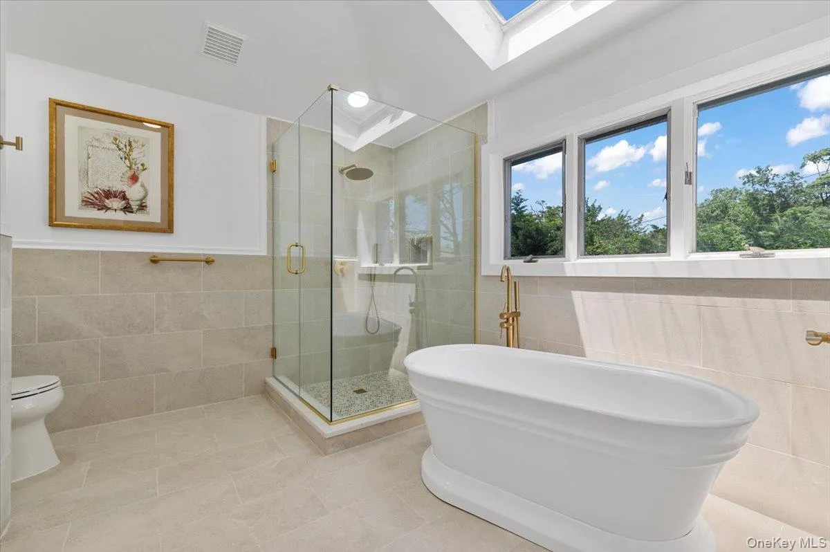 Bathroom with tile walls, a skylight, tile patterned flooring, a shower stall, and a freestanding tub Bathroom with tile walls, a skylight, tile patterned flooring, a shower stall, and a freestanding tub