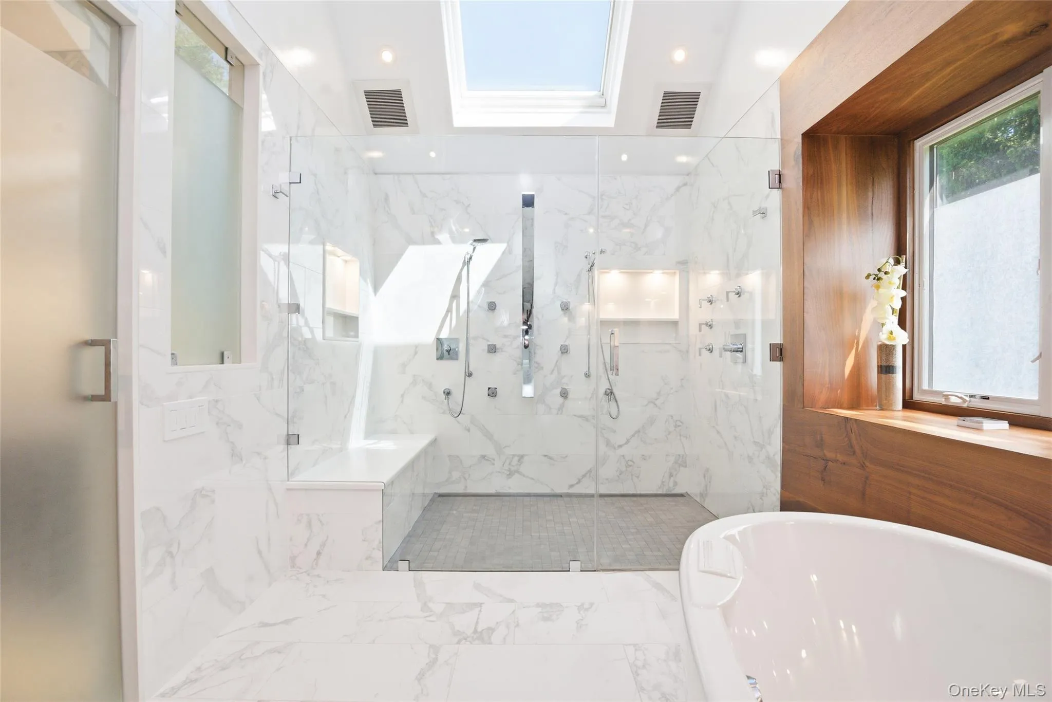 Light-filled primary bath showcasing a seamless glass shower, soaking tub, and timeless designer finishes throughout. Light-filled primary bath showcasing a seamless glass shower, soaking tub, and timeless designer finishes throughout.