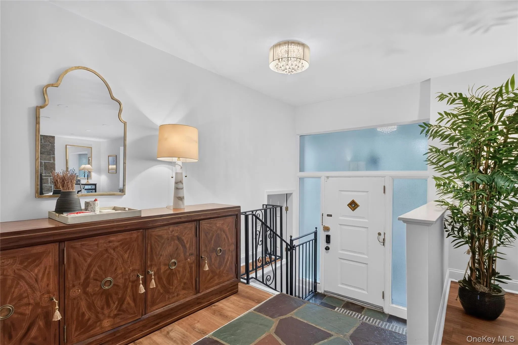 Entryway featuring a white paneled door with frosted sidelights and transom, chandelier lighting, wood-finish flooring, and a stone tile landing Entryway featuring a white paneled door with frosted sidelights and transom, chandelier lighting, wood-finish flooring, and a stone tile landing